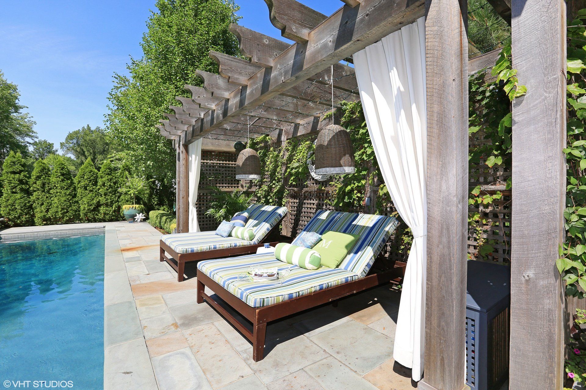 Two lounge chairs under a pergola next to a pool