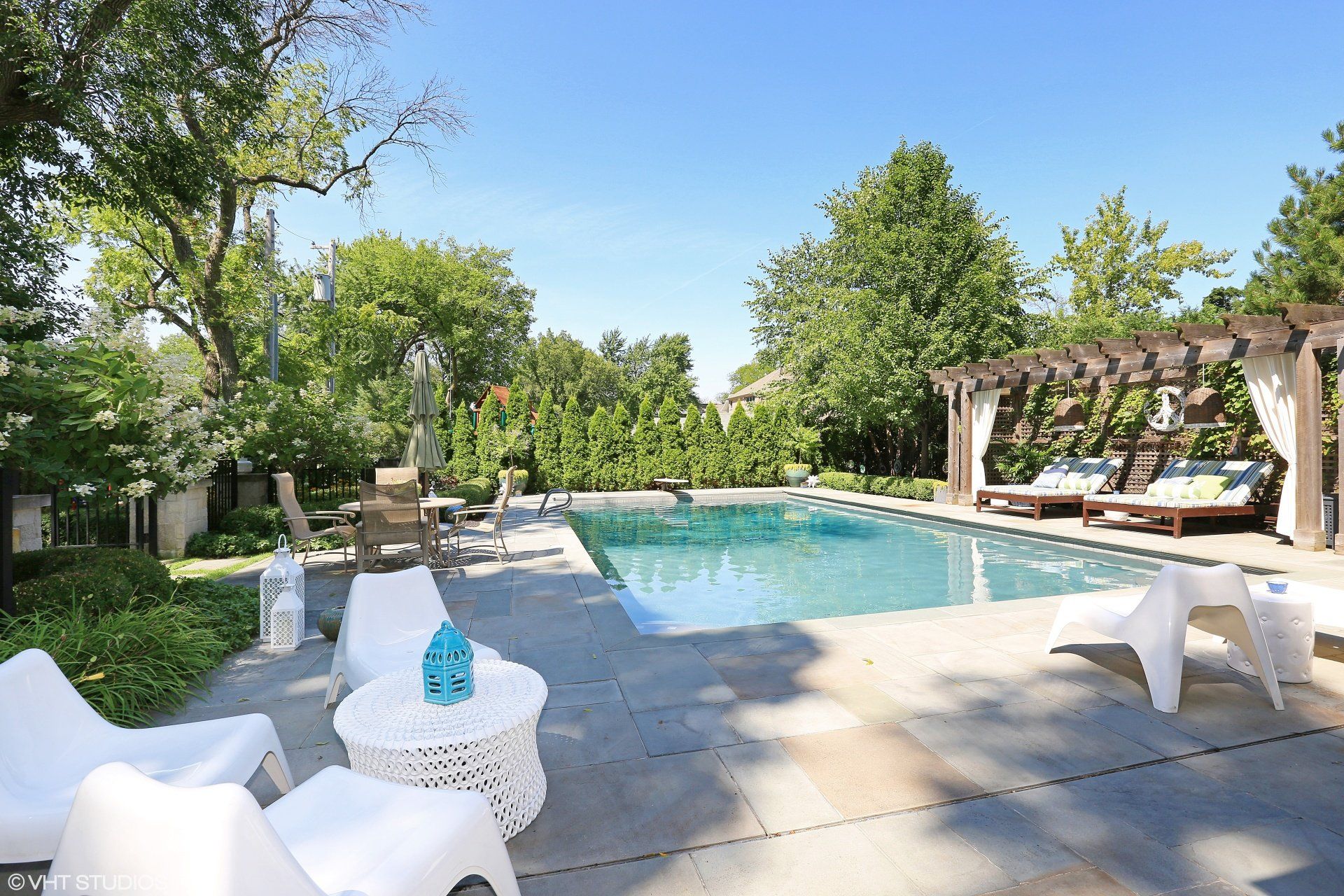 A large swimming pool with a pergola and chairs around it