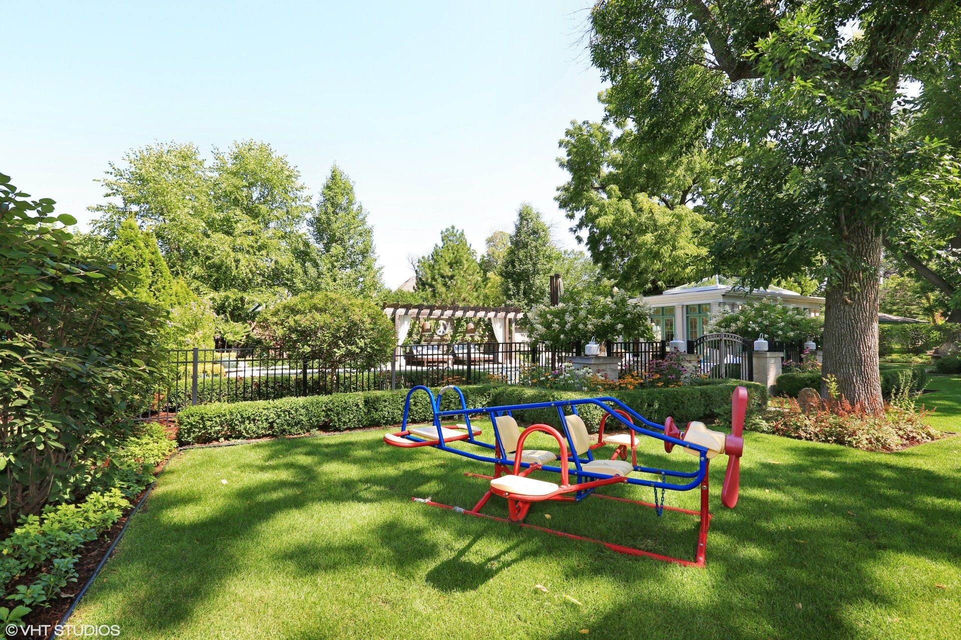 A red , white and blue seesaw is in the middle of a lush green yard.