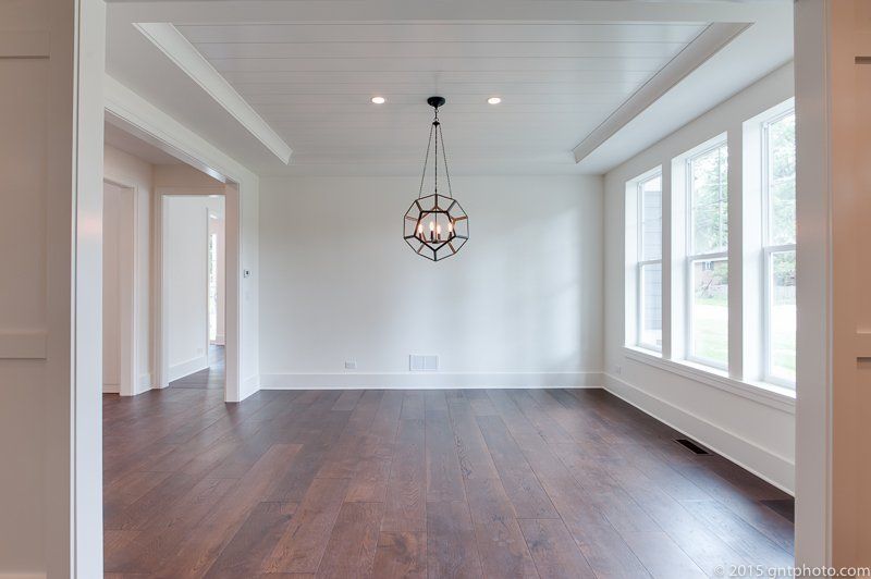 An empty living room with hardwood floors and a chandelier hanging from the ceiling.