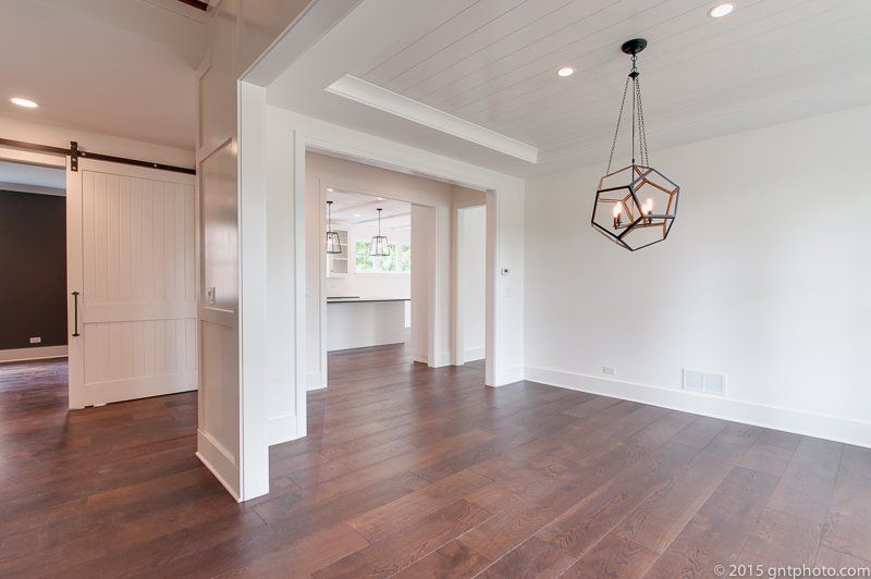An empty room with hardwood floors and a chandelier hanging from the ceiling.