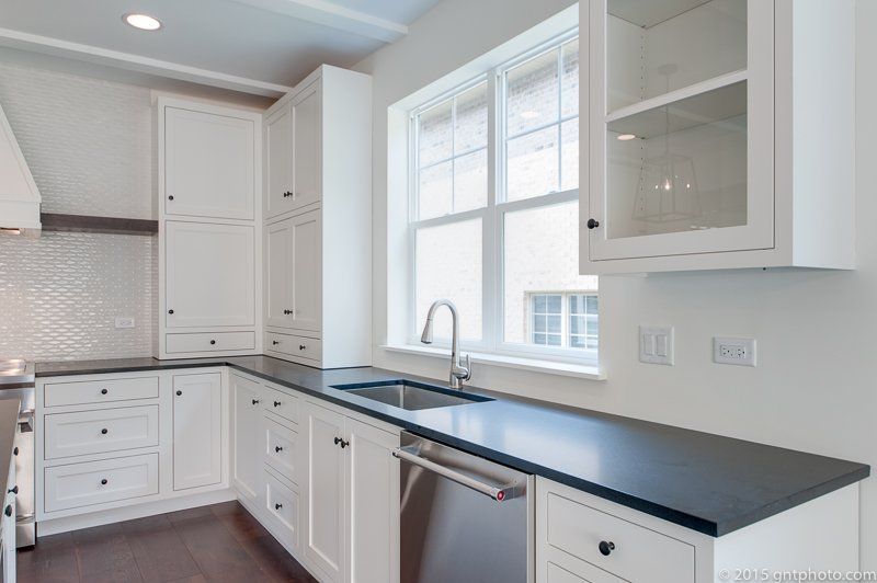 A kitchen with white cabinets , black counter tops , a sink and a window.