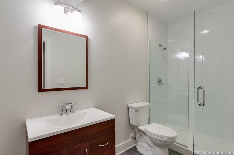 A bathroom with a toilet , sink , mirror and walk in shower.