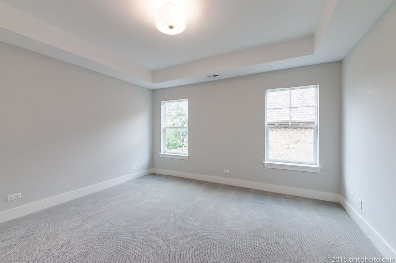 An empty bedroom with two windows and a ceiling fan.