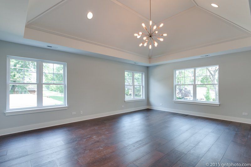 A large empty room with hardwood floors and a chandelier hanging from the ceiling.