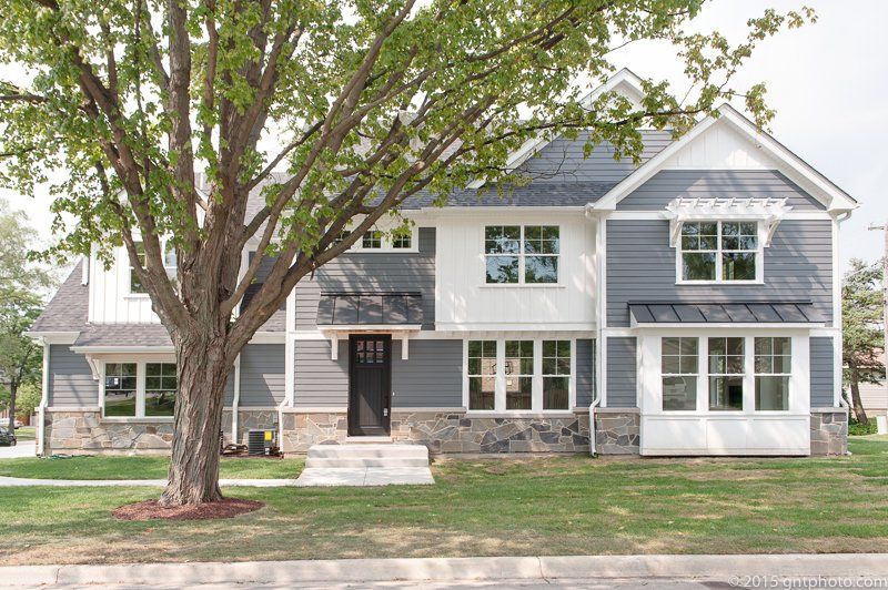 A large gray and white house with a tree in front of it.