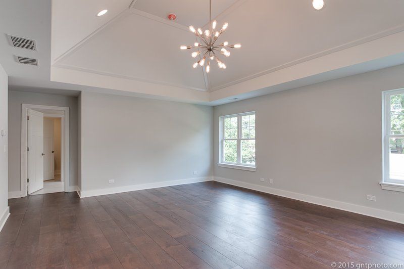 A large empty room with hardwood floors and a chandelier hanging from the ceiling.