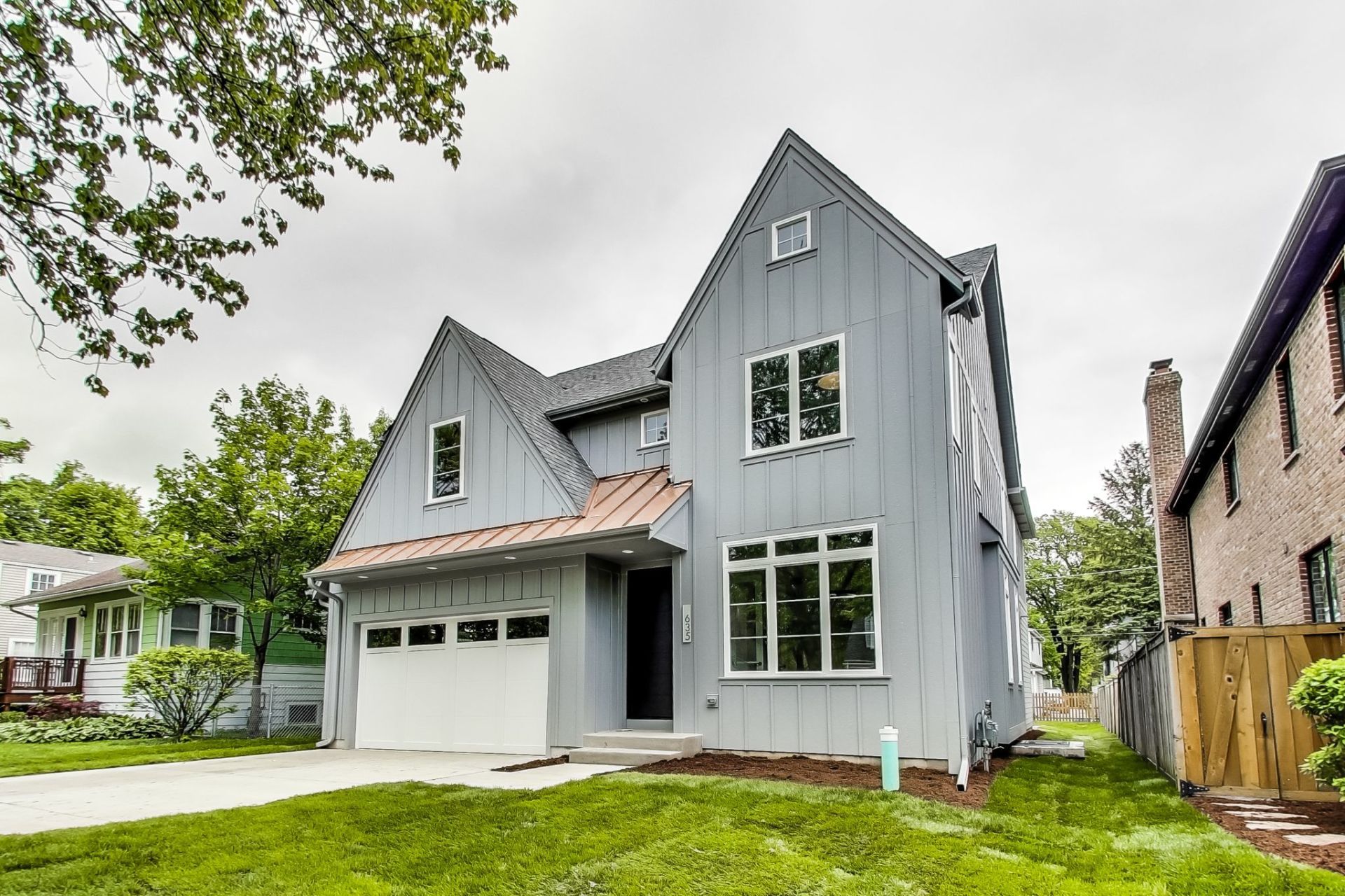 A large gray house with a white garage door is sitting on top of a lush green lawn.