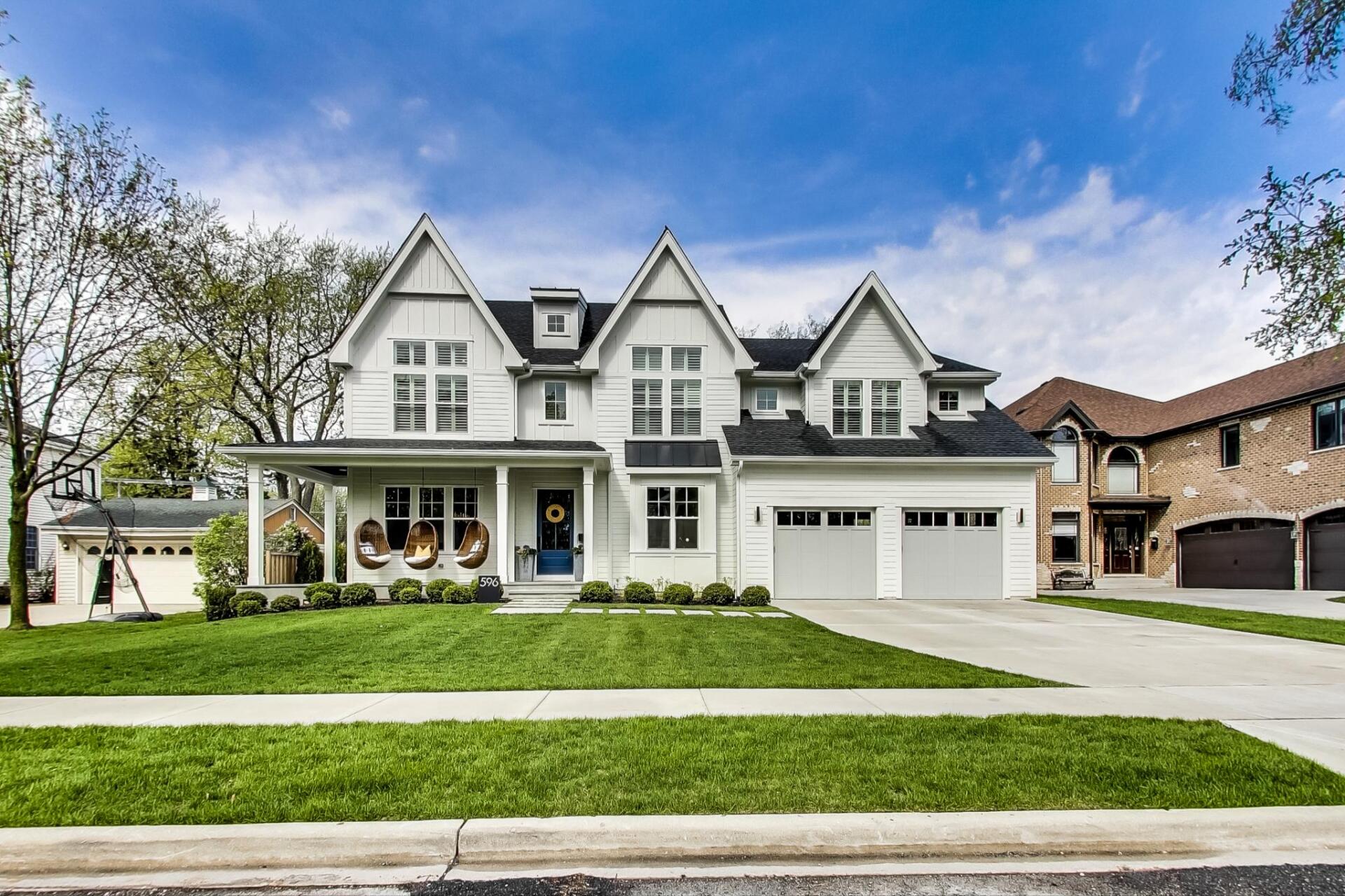 A large white house with a black roof is sitting on top of a lush green lawn.