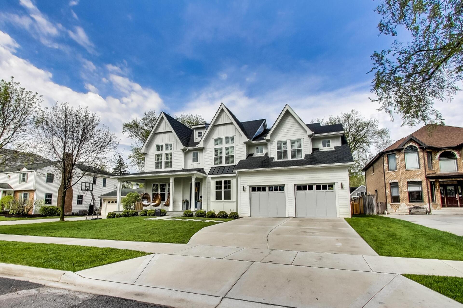 A large white house with a black roof is in a residential neighborhood.