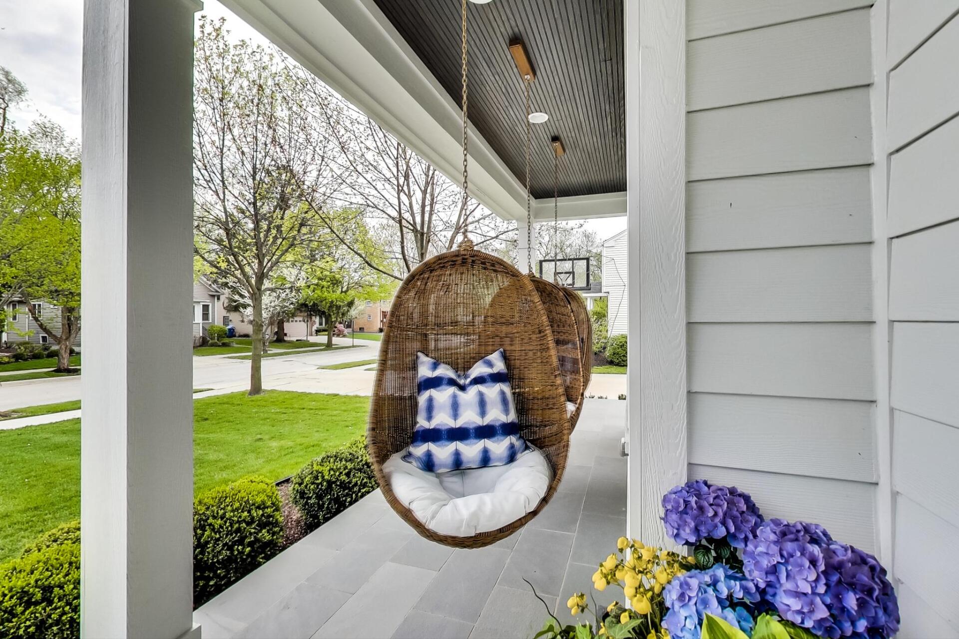A porch with a wicker chair hanging from the ceiling.