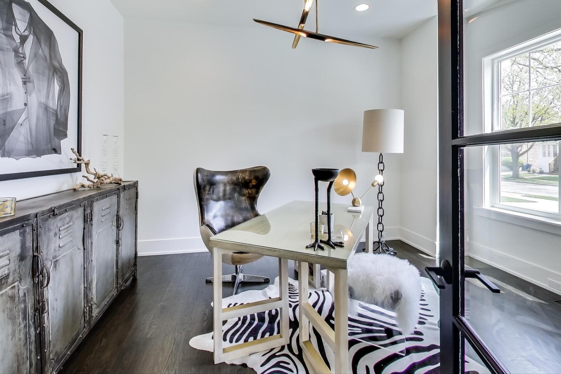 A home office with a desk , chair , lamp and zebra print rug.