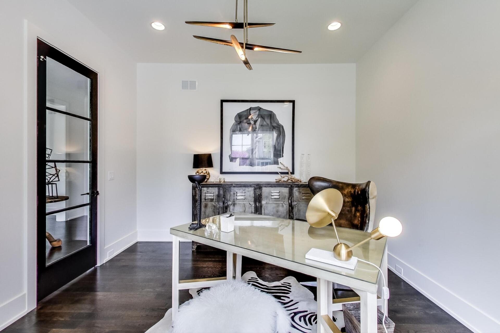 A home office with a desk , chairs , and a picture on the wall.