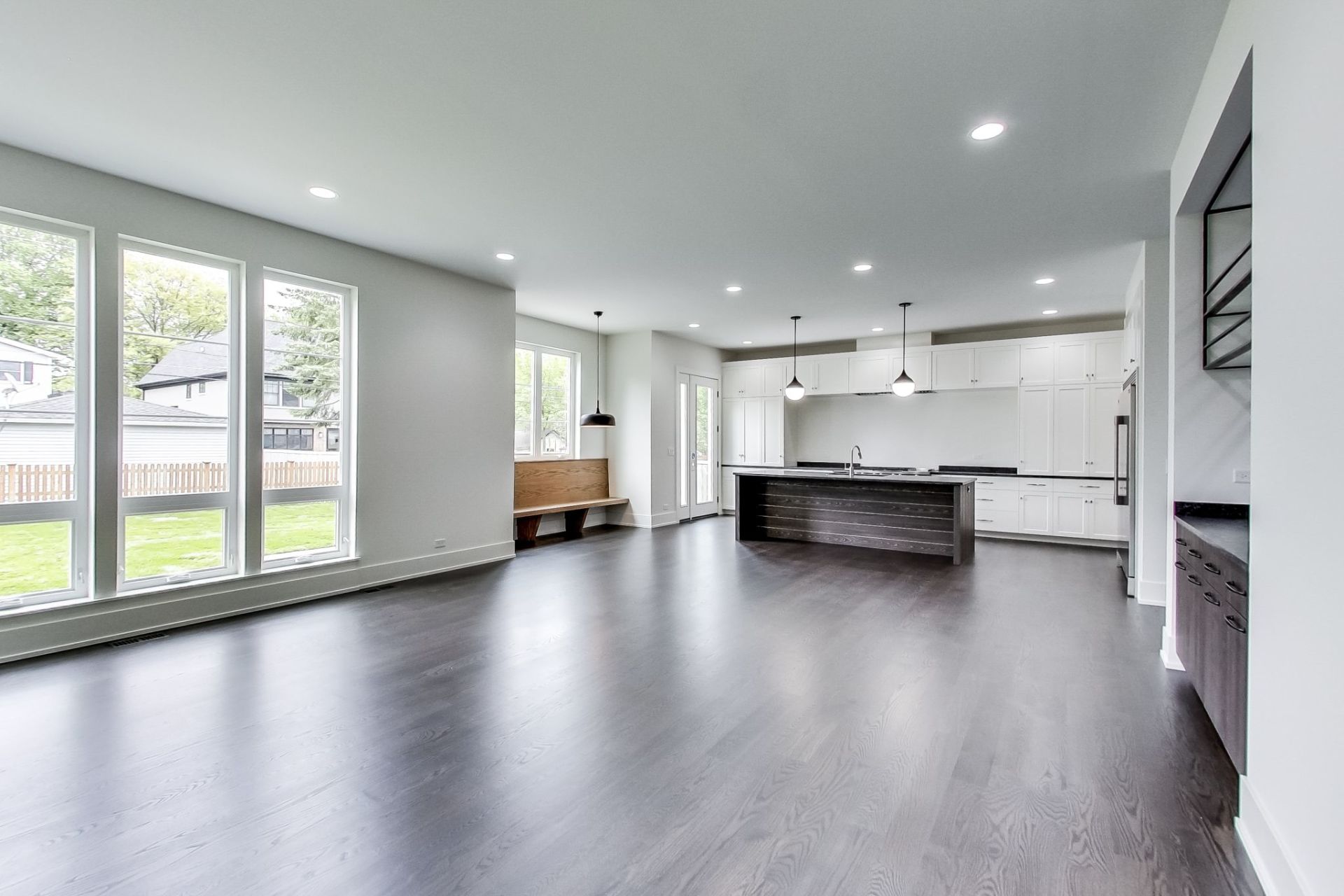 An empty living room with hardwood floors and a kitchen in the background.