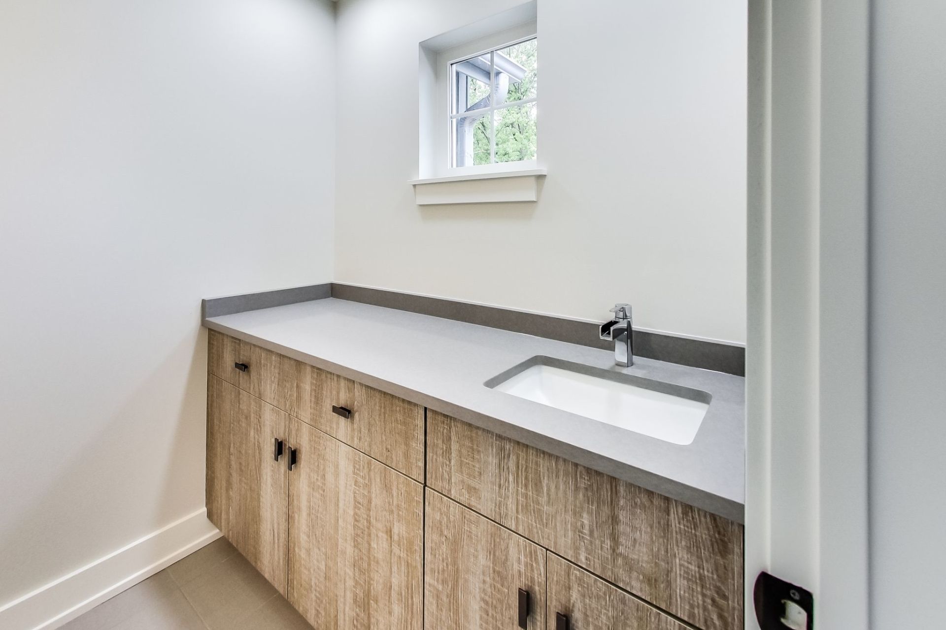 A bathroom with a sink , cabinets , and a window.