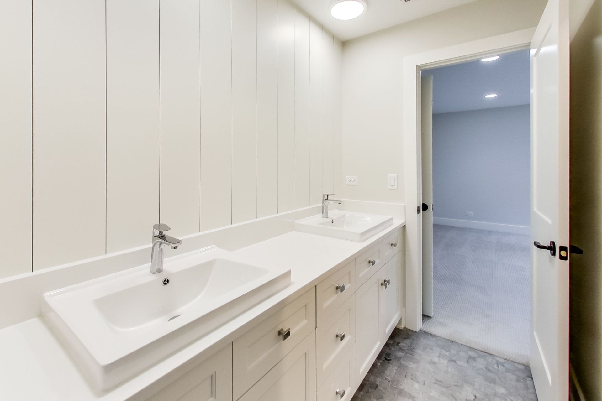 A bathroom with two sinks and a door leading to a bedroom.