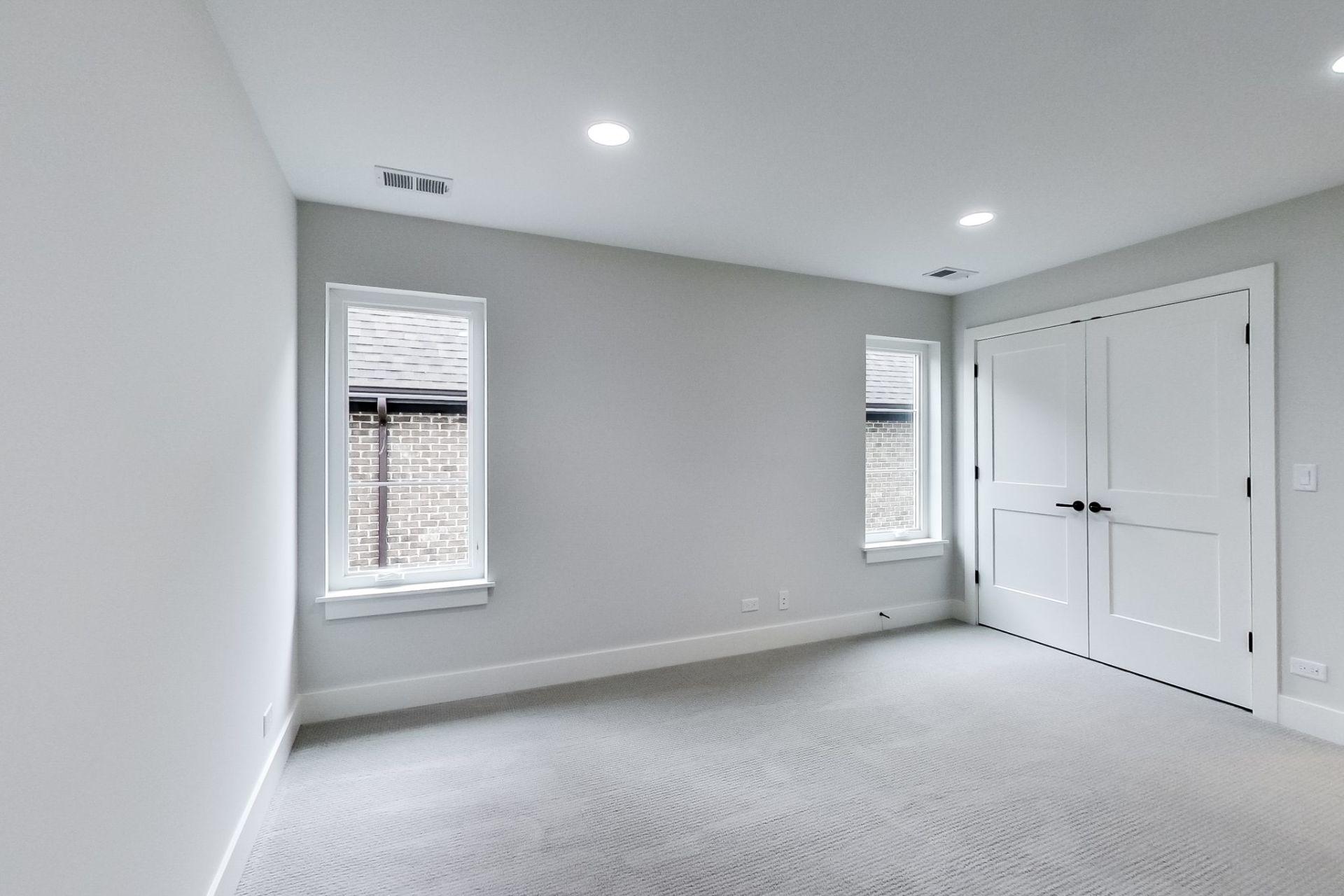 An empty room with a carpeted floor and two windows.