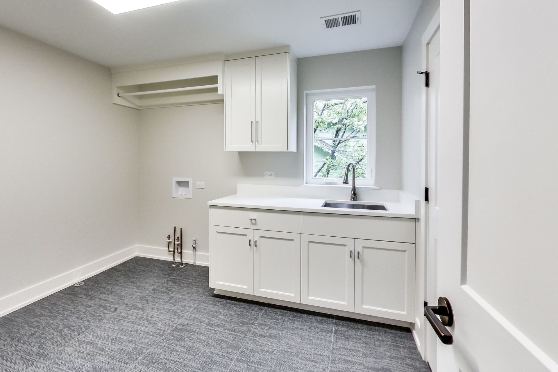 A laundry room with white cabinets , a sink , and a window.