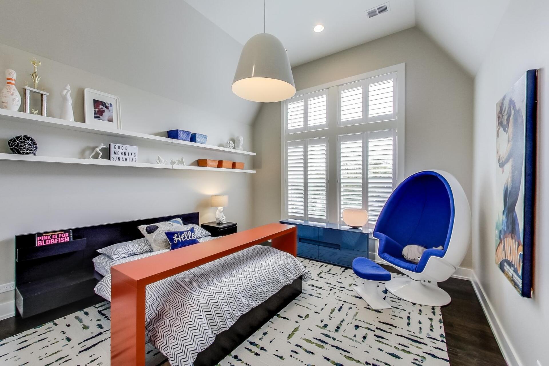 A bedroom with a bed , chairs , shelves and a window.