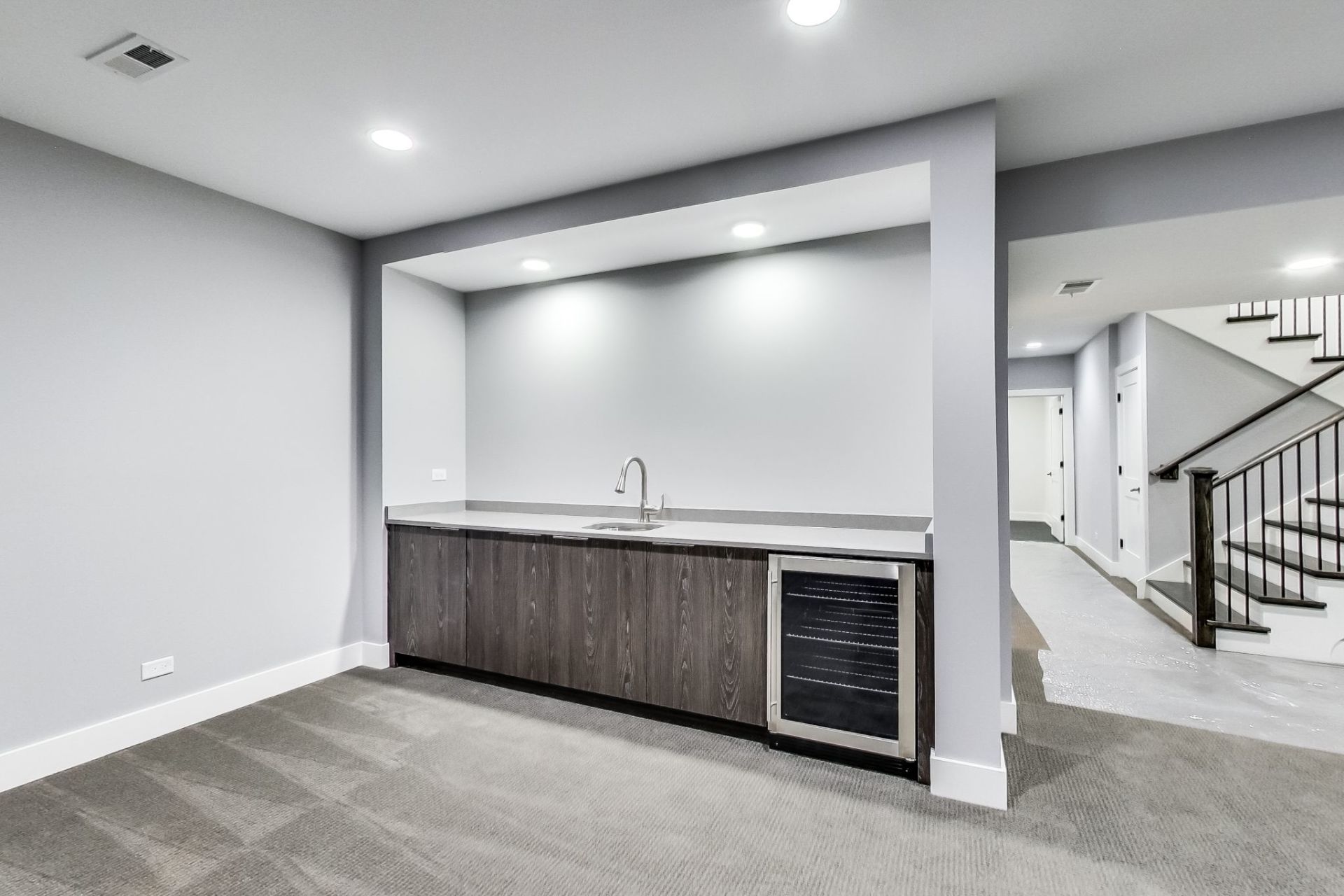 An empty basement with a bar and a refrigerator.