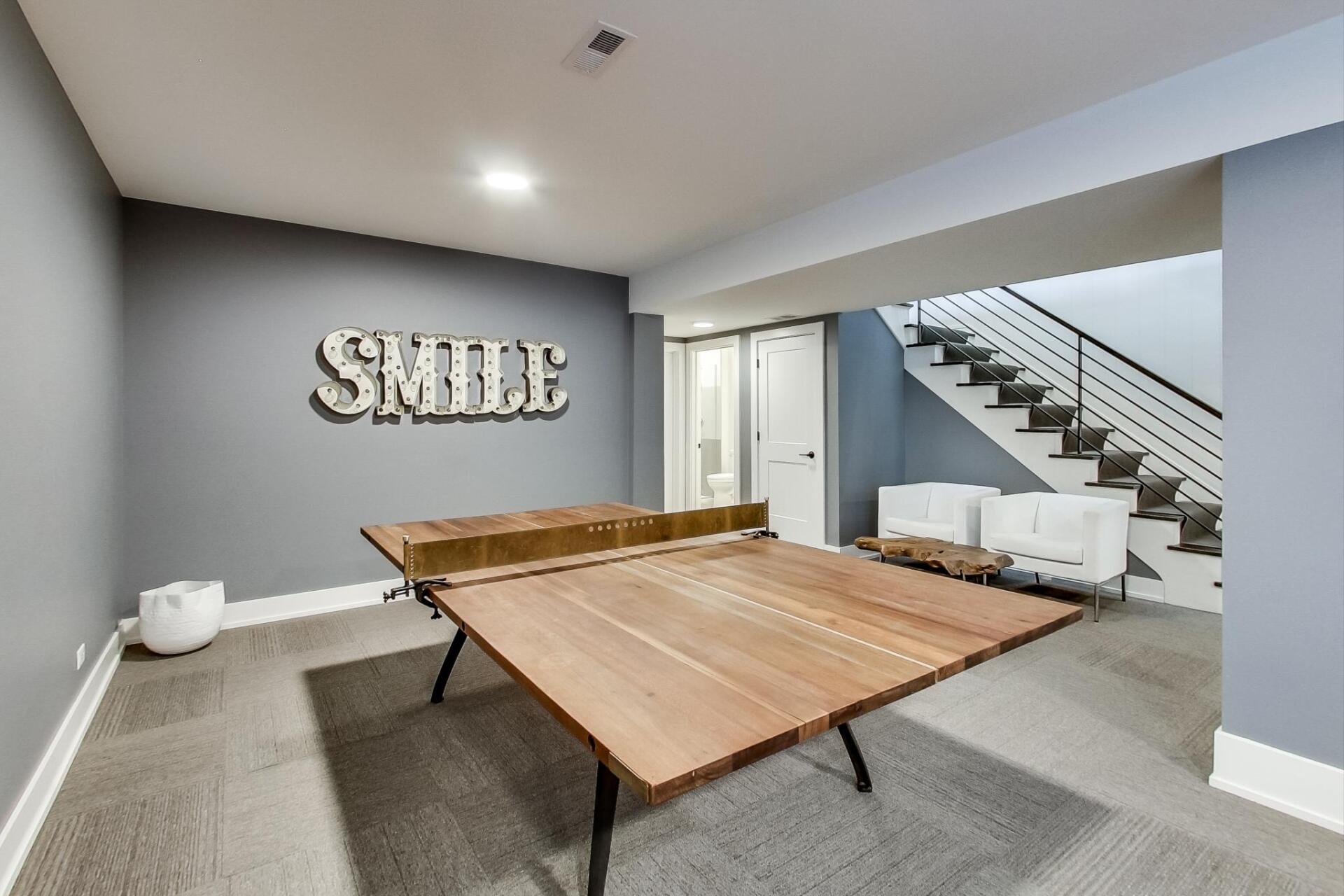 A basement with a ping pong table and stairs.
