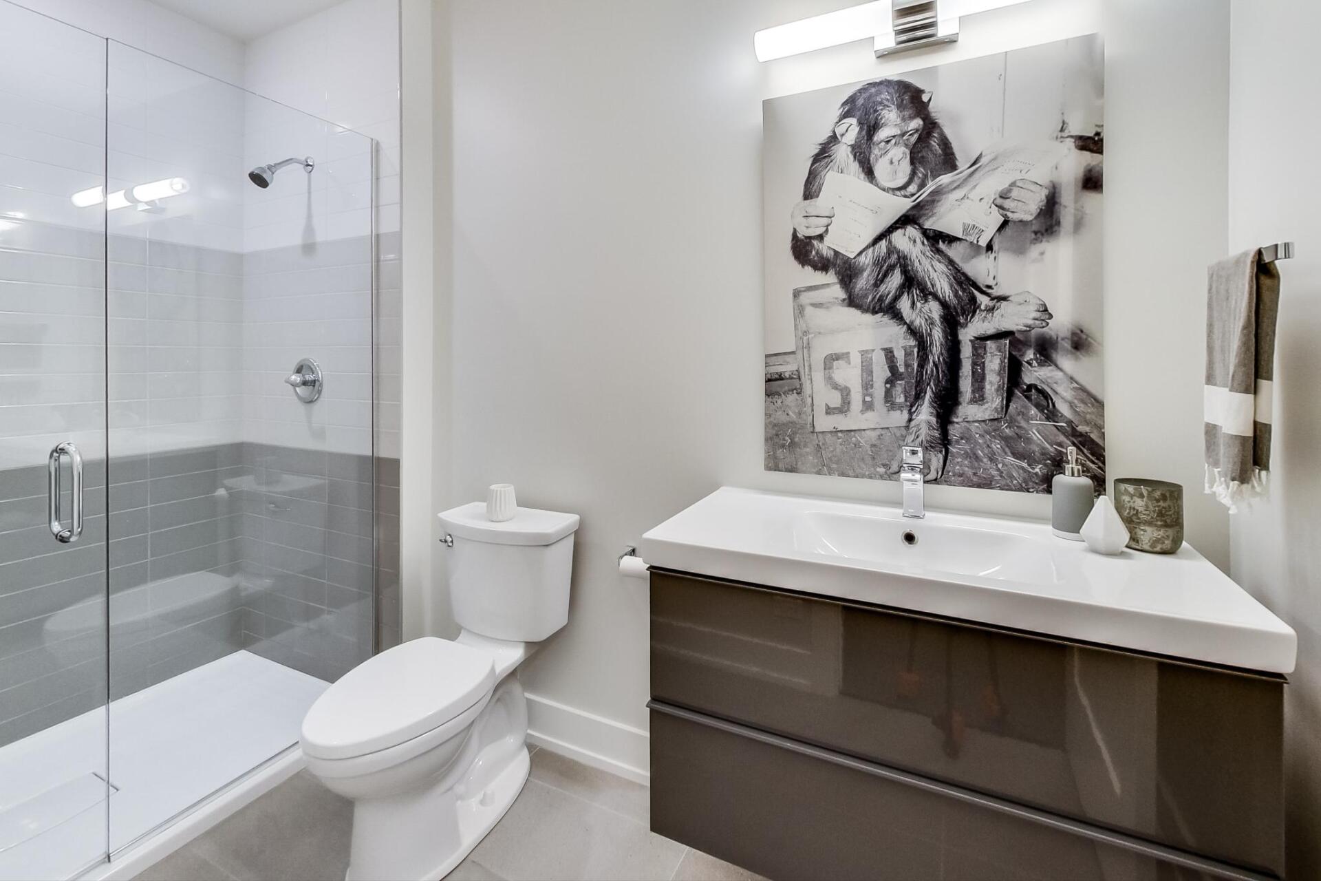 A bathroom with a toilet , sink , shower and a painting on the wall.