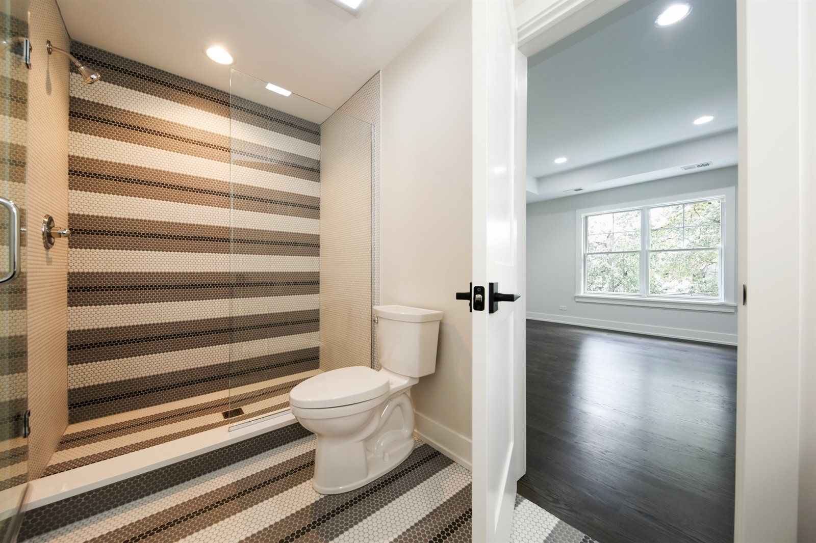 A bathroom with a toilet , shower and striped wall.