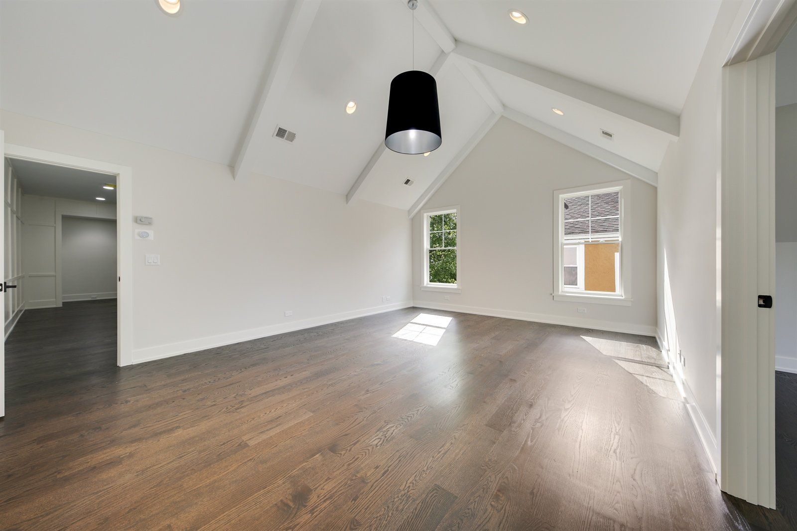 An empty room with hardwood floors and a vaulted ceiling.