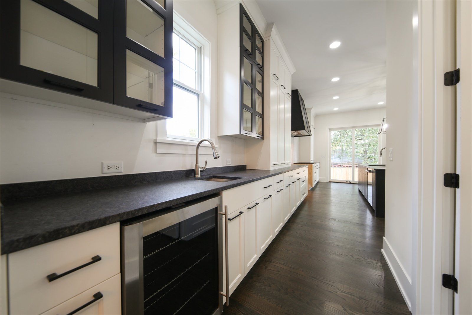 A kitchen with black counter tops and white cabinets and a wine cooler.