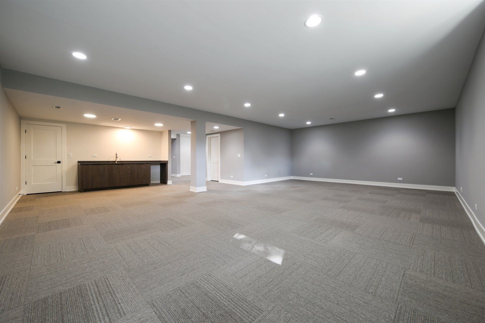 An empty basement with a carpeted floor and a bar.