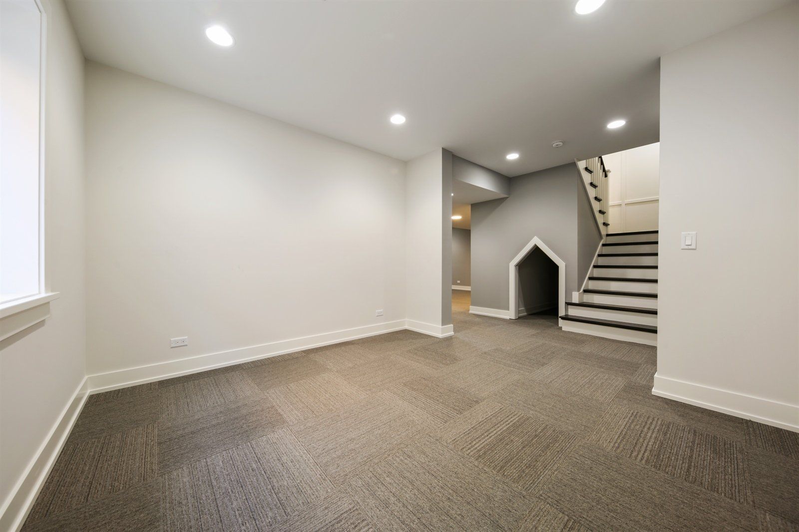 An empty basement with a dog house and stairs.