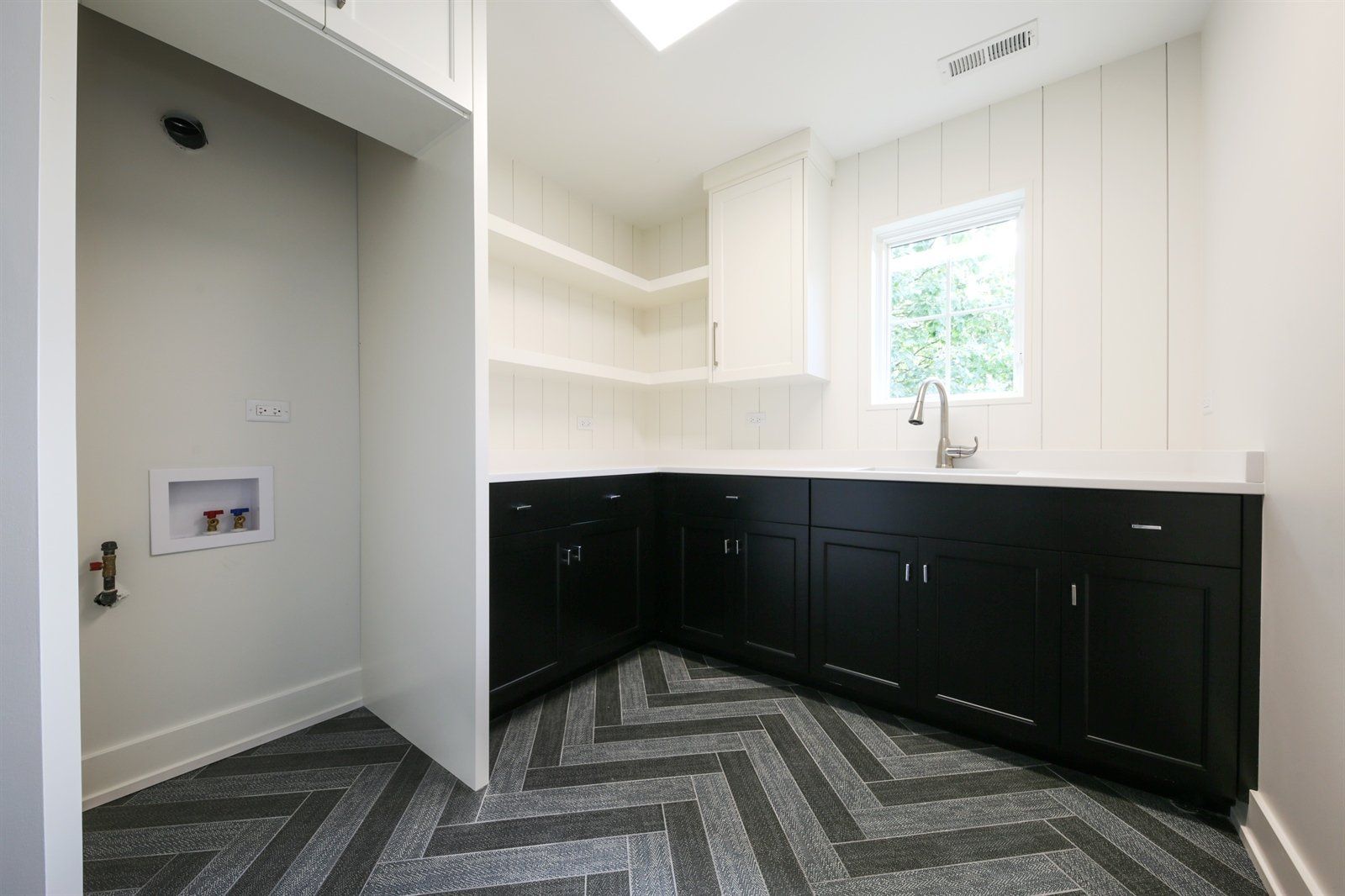 A laundry room with black cabinets and a herringbone floor.