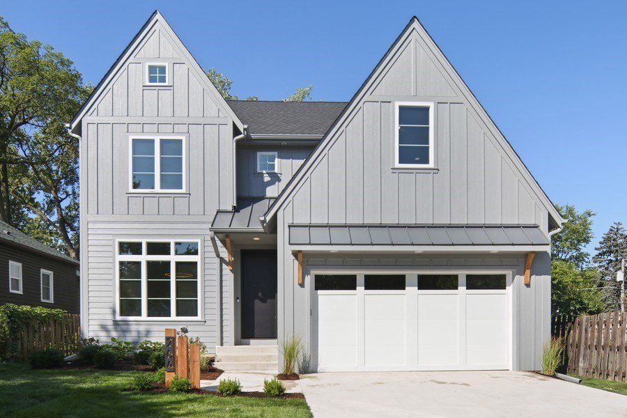 A large gray house with a white garage door and a black roof.