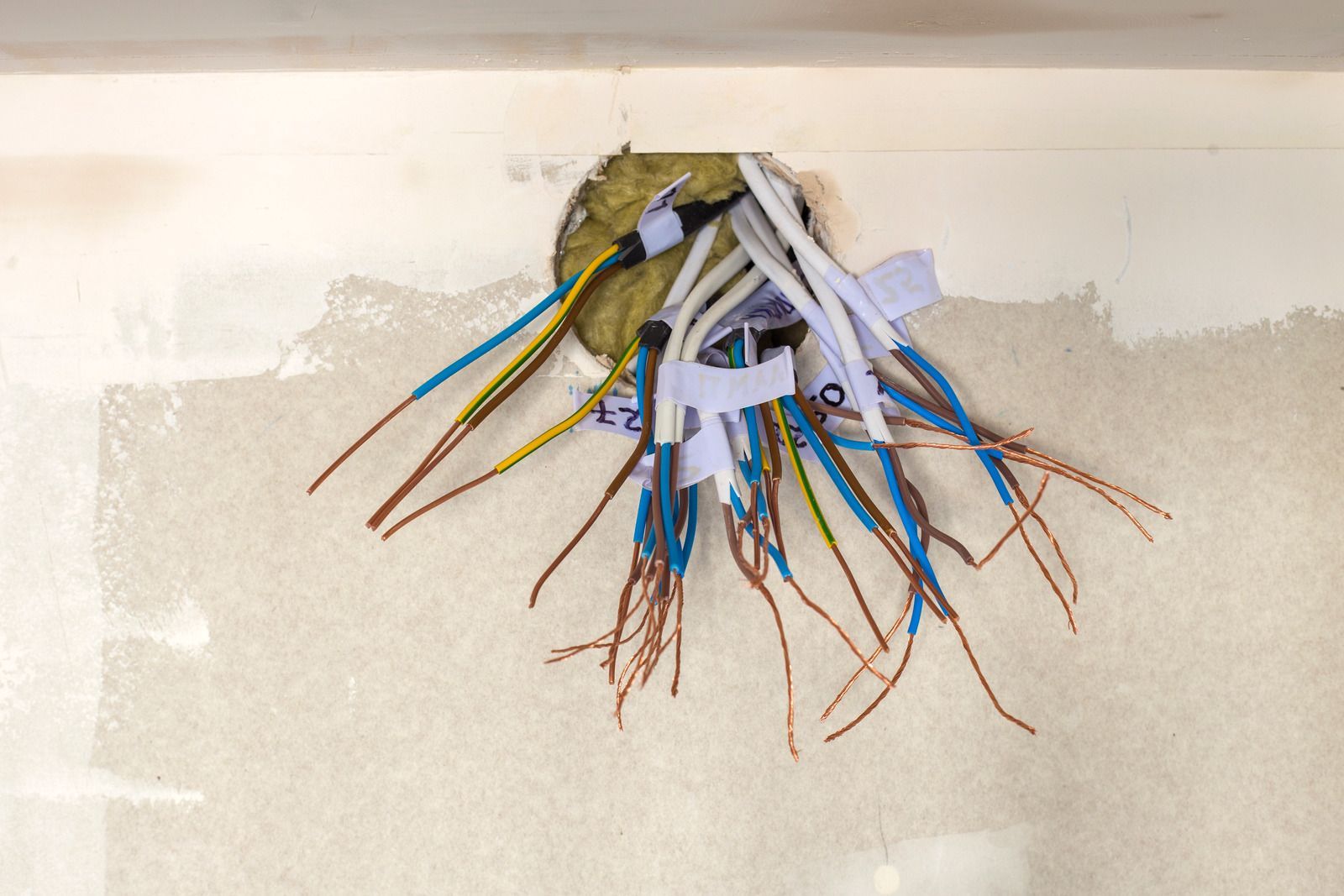 A bunch of wires are coming out of a hole in the wall.