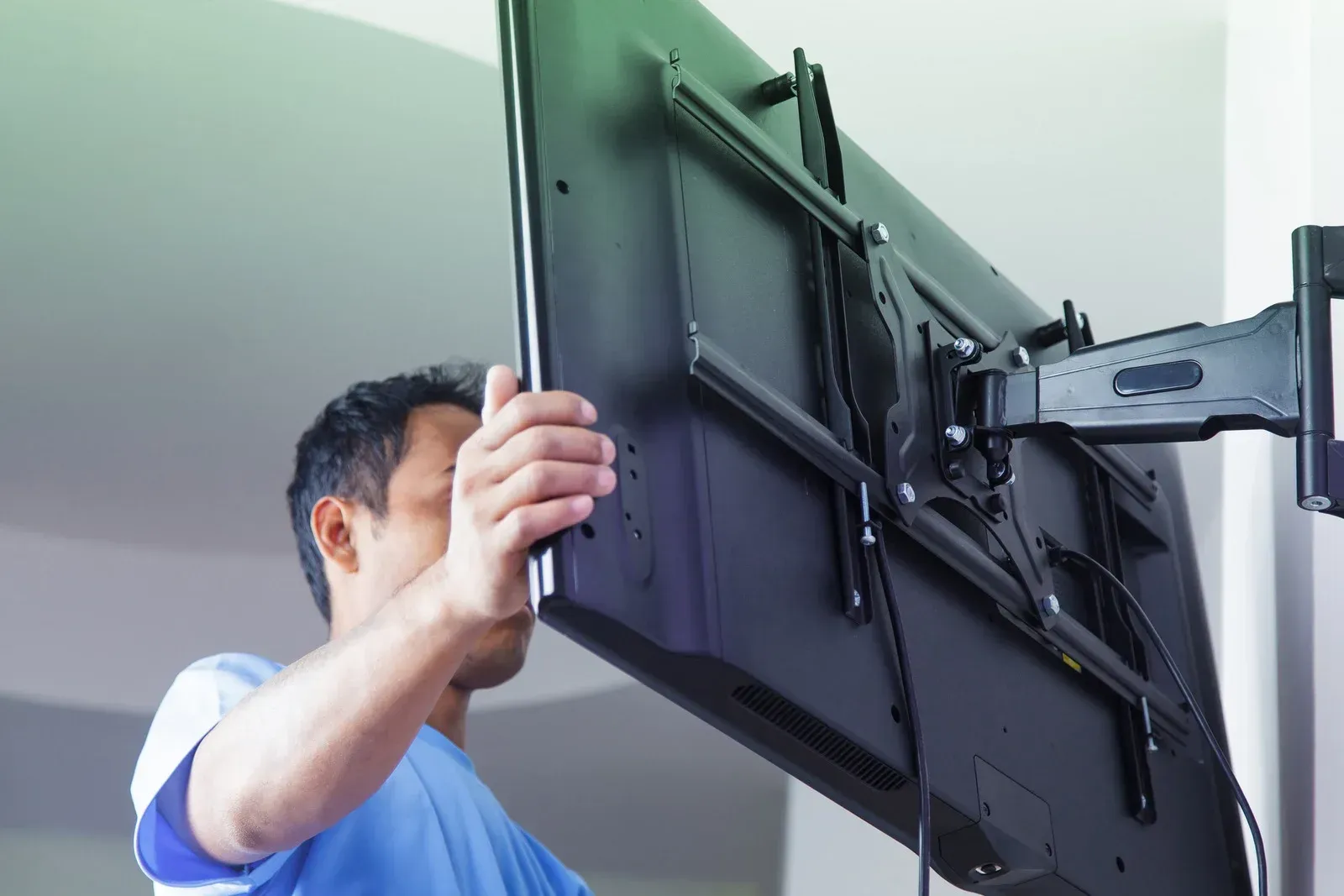 A man is installing a flat screen tv on a wall mount.