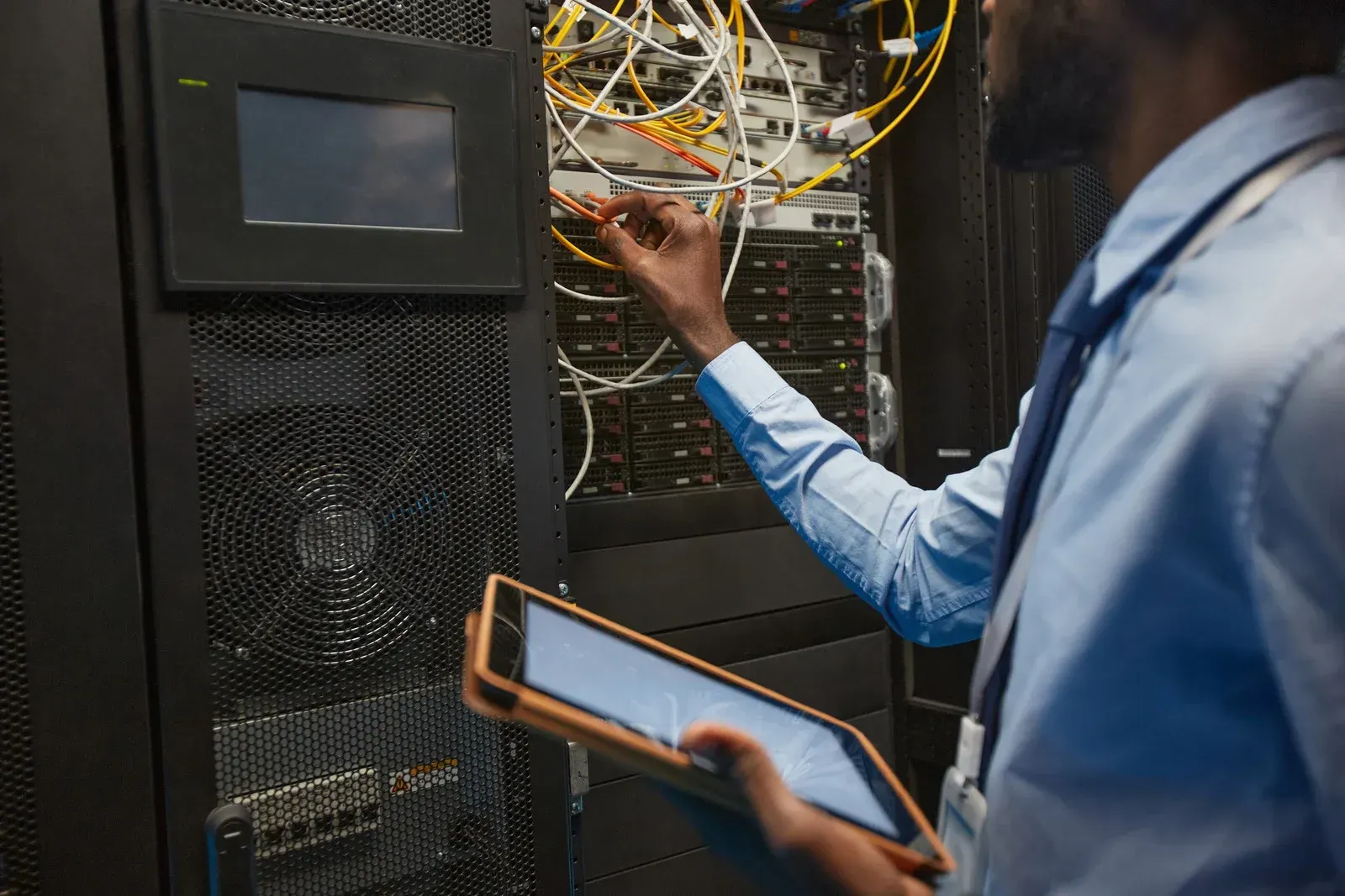 A man is working on a server in a data center while holding a tablet.