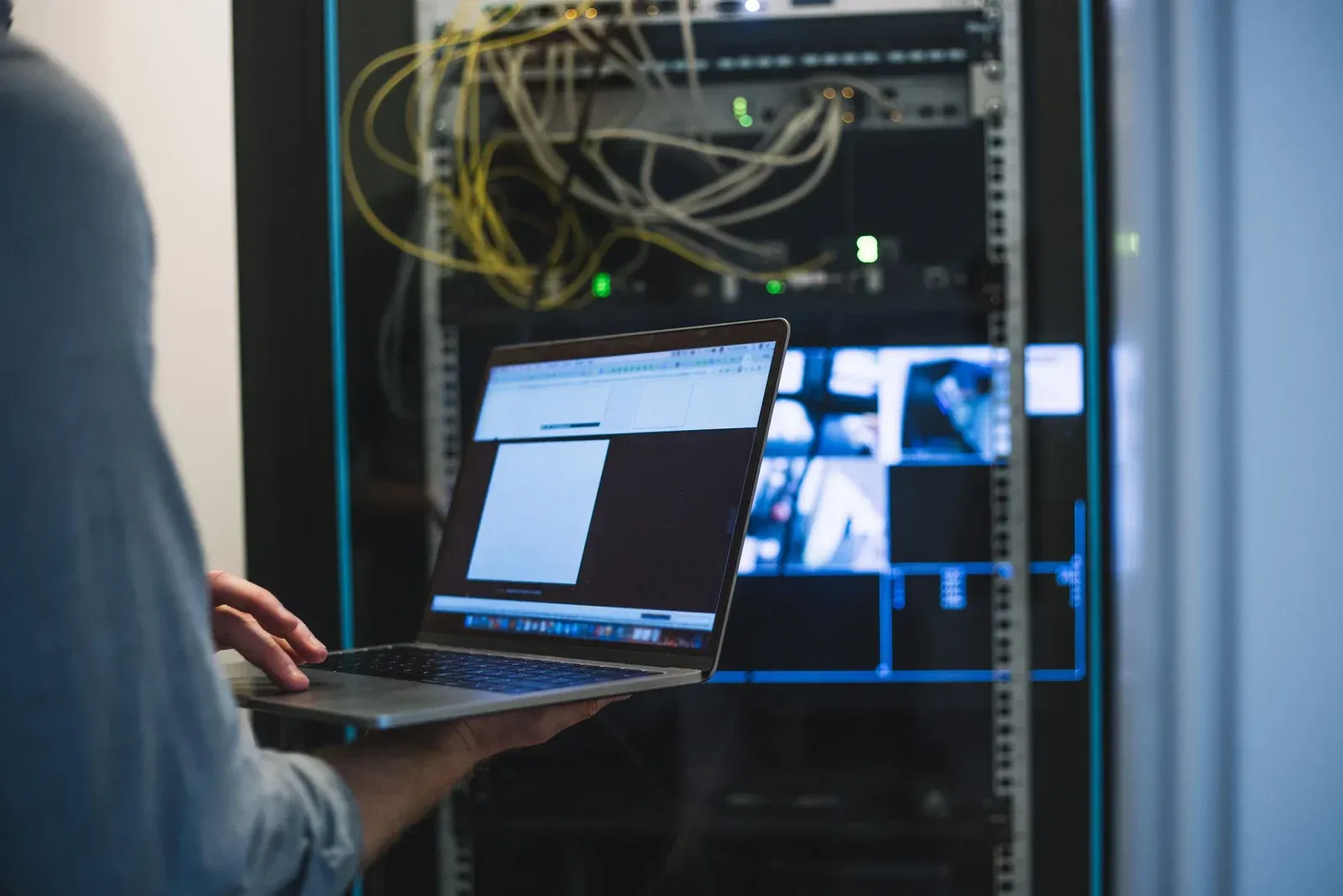 A man is holding a laptop in a server room.