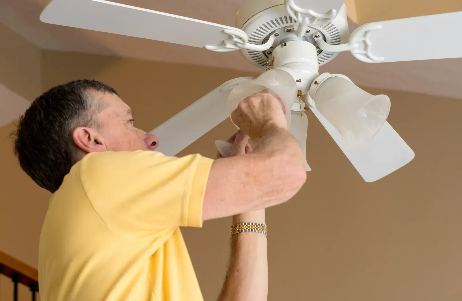 A man in a yellow shirt is fixing a ceiling fan