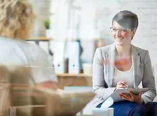 A Woman Is Sitting In A Chair Talking To Another Woman While Holding A Clipboard - Phoenix, AZ - Infinite Healing and Wellness