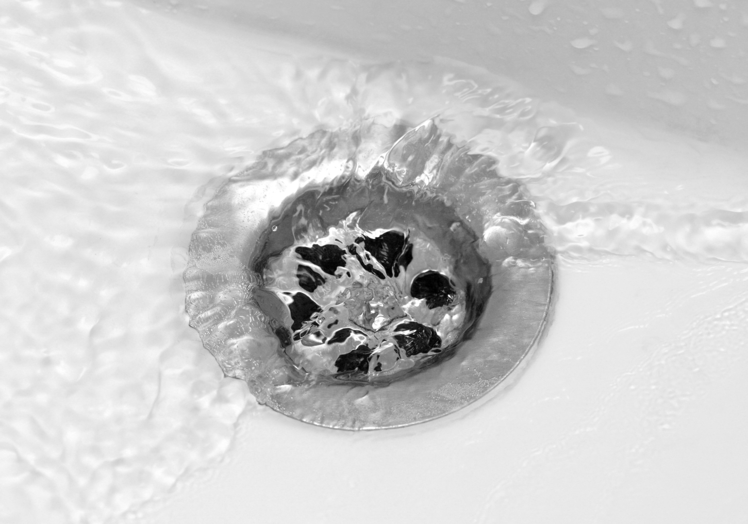 A black and white photo of a sink drain with water running down it.