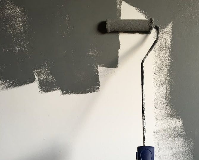 A paint roller is being used to paint a wall.