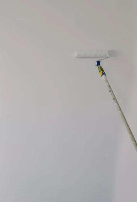 A paint roller is being used to paint a white wall.
