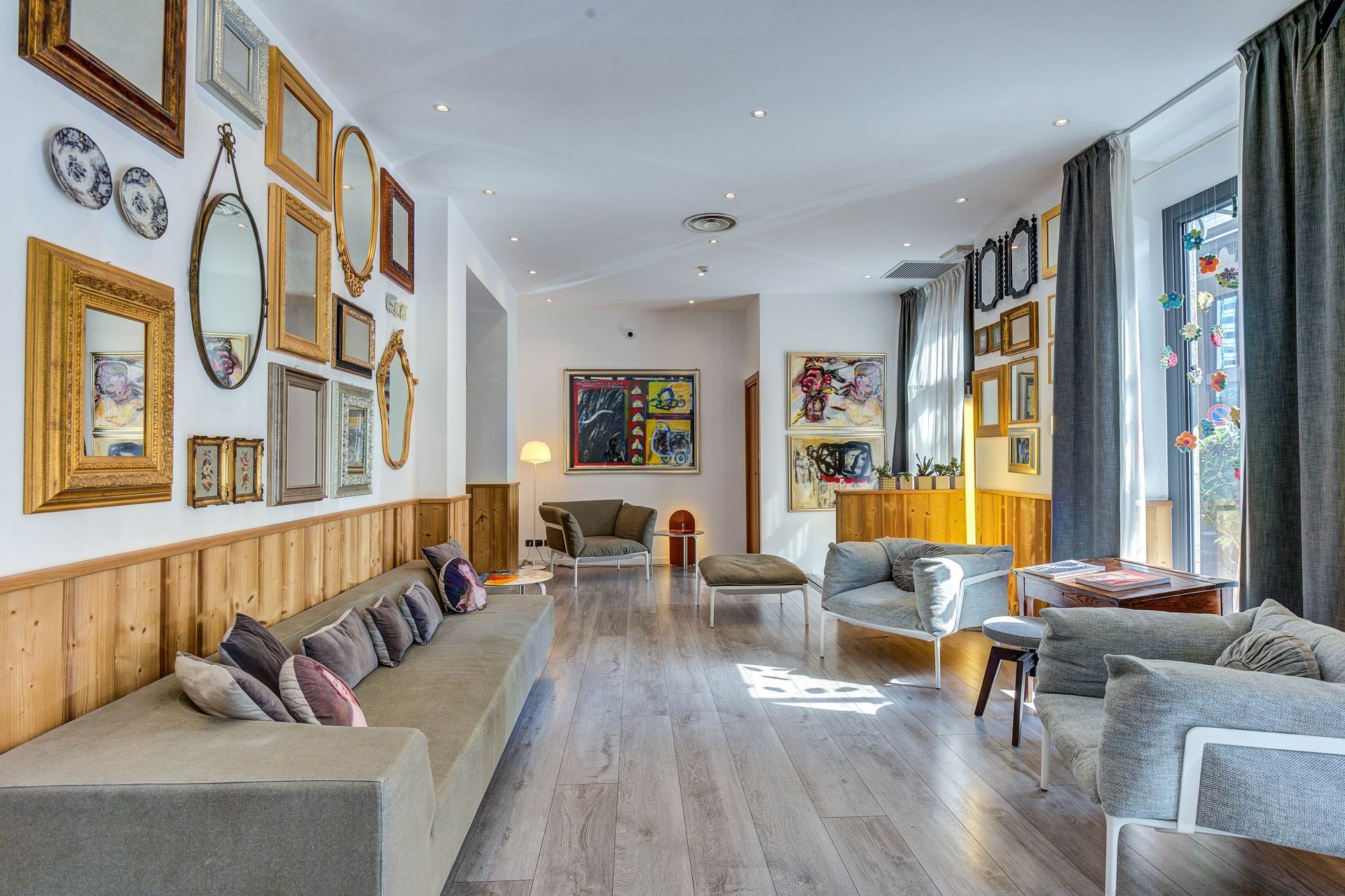 A modern lounge with eclectic decor: Mirrors, art, gray sofas, wooden accents, and large windows.