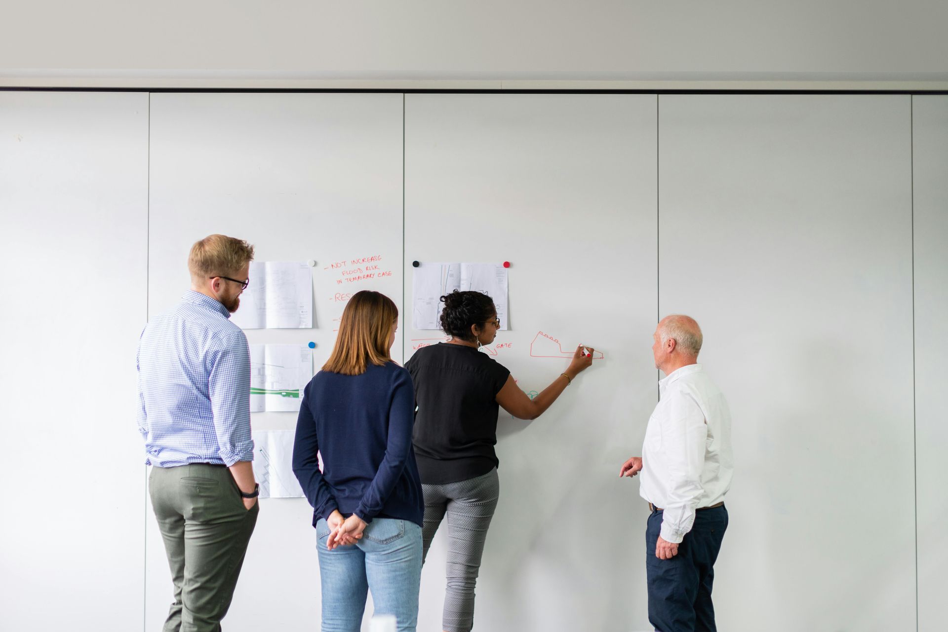 Four people stand before a whiteboard, reviewing and annotating notes.