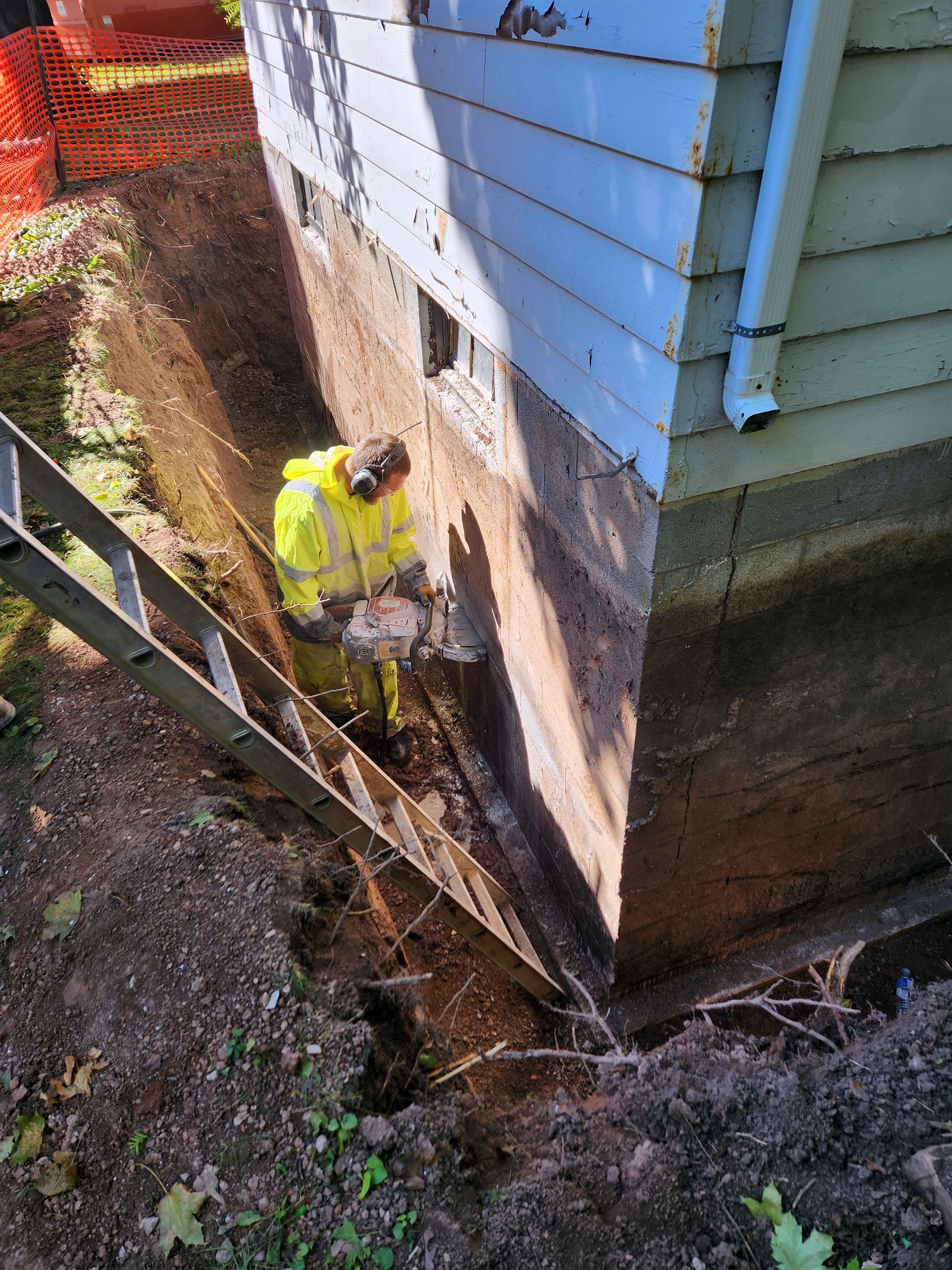 Worker in yellow suit using tool to work on foundation of a building.