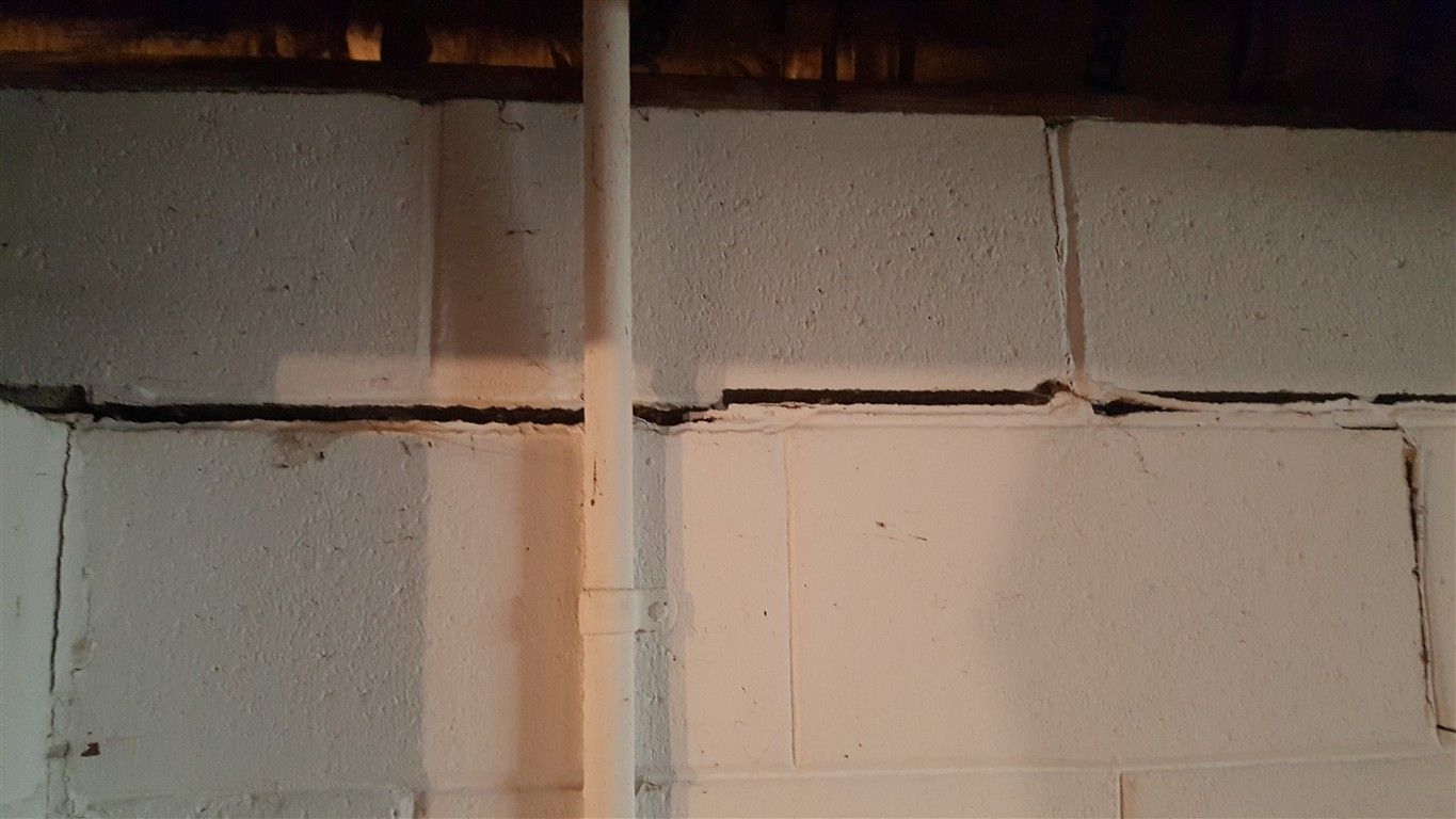 White painted concrete block basement wall with visible cracks and a vertical pipe.