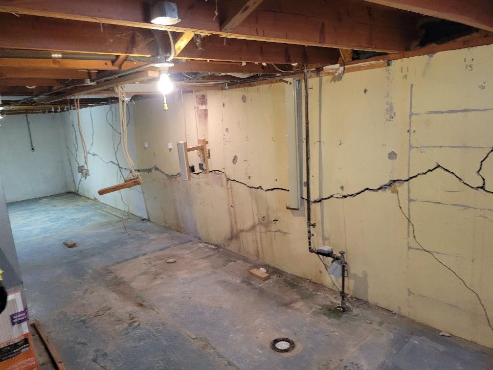 Basement interior with cracked concrete walls and exposed ceiling beams.