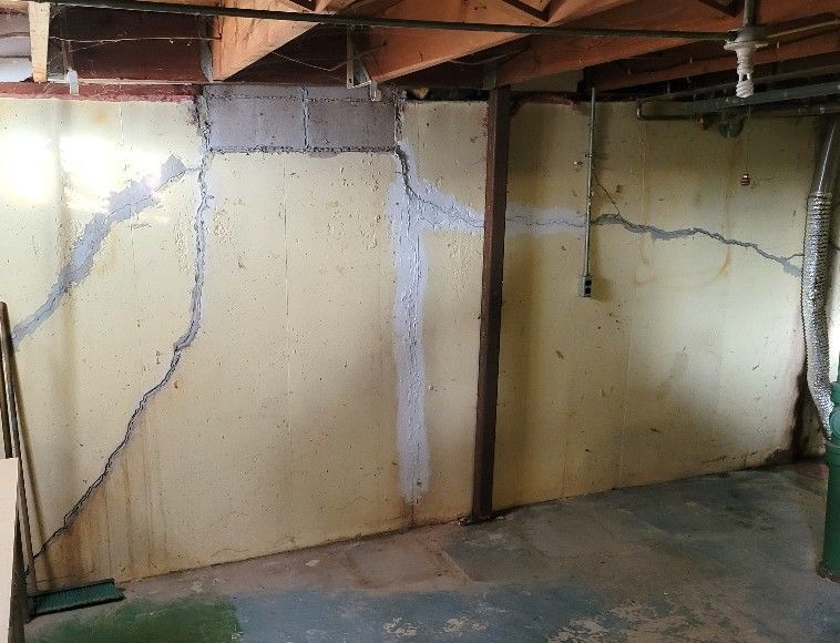 Basement wall with large cracks and patched areas, dark stained from moisture.