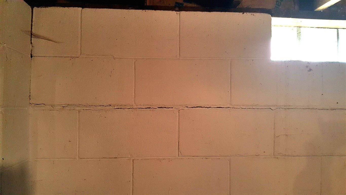 White painted concrete block wall with a small window, likely in a basement.