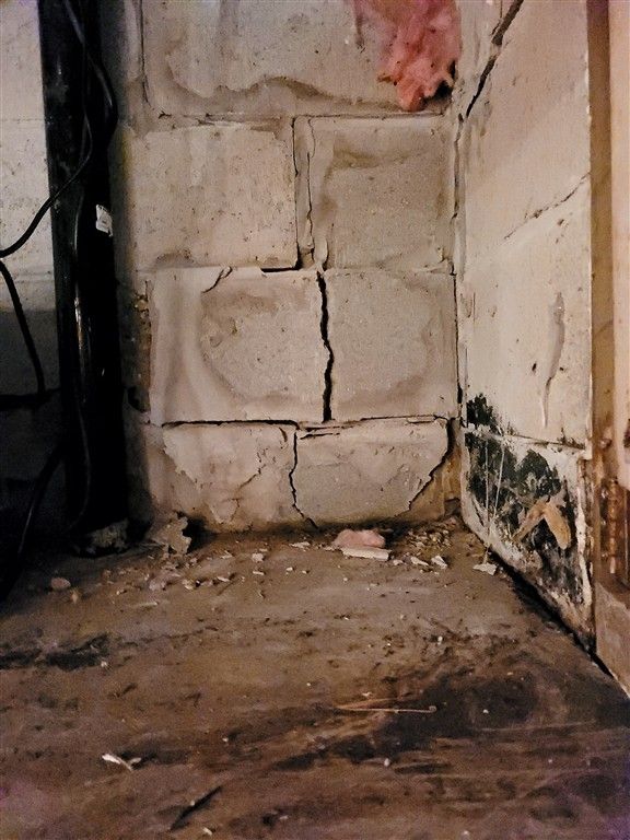 Cracked concrete block wall in a basement corner, showing signs of water damage and mold.